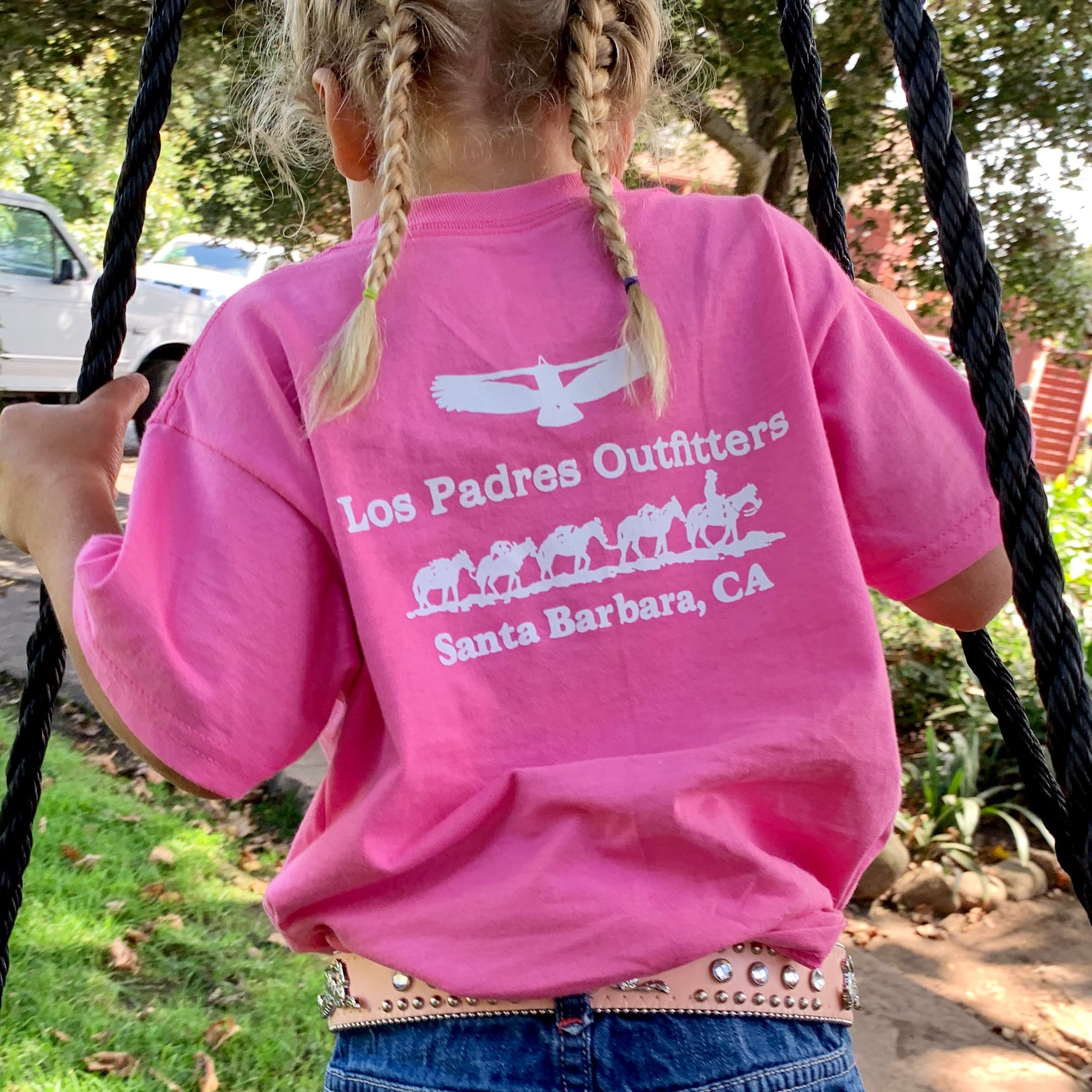 Back view of little girl outside wearing the comfortable pink cotton Kids Short Sleeve Tee with the Los Padres Outfitters logo on the back