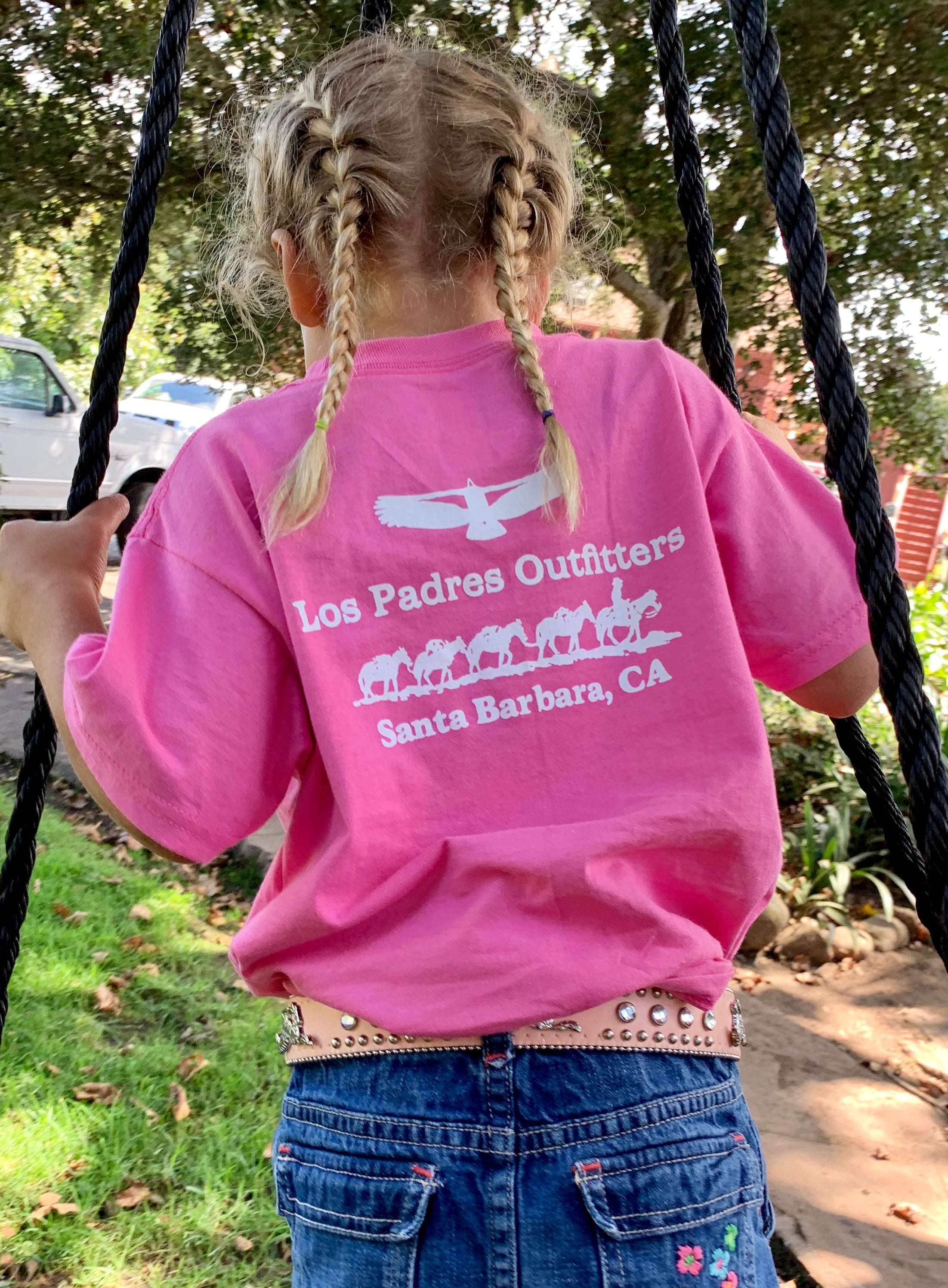Back view of little girl outside wearing the comfortable pink cotton Kids Short Sleeve Tee with the Los Padres Outfitters logo on the back