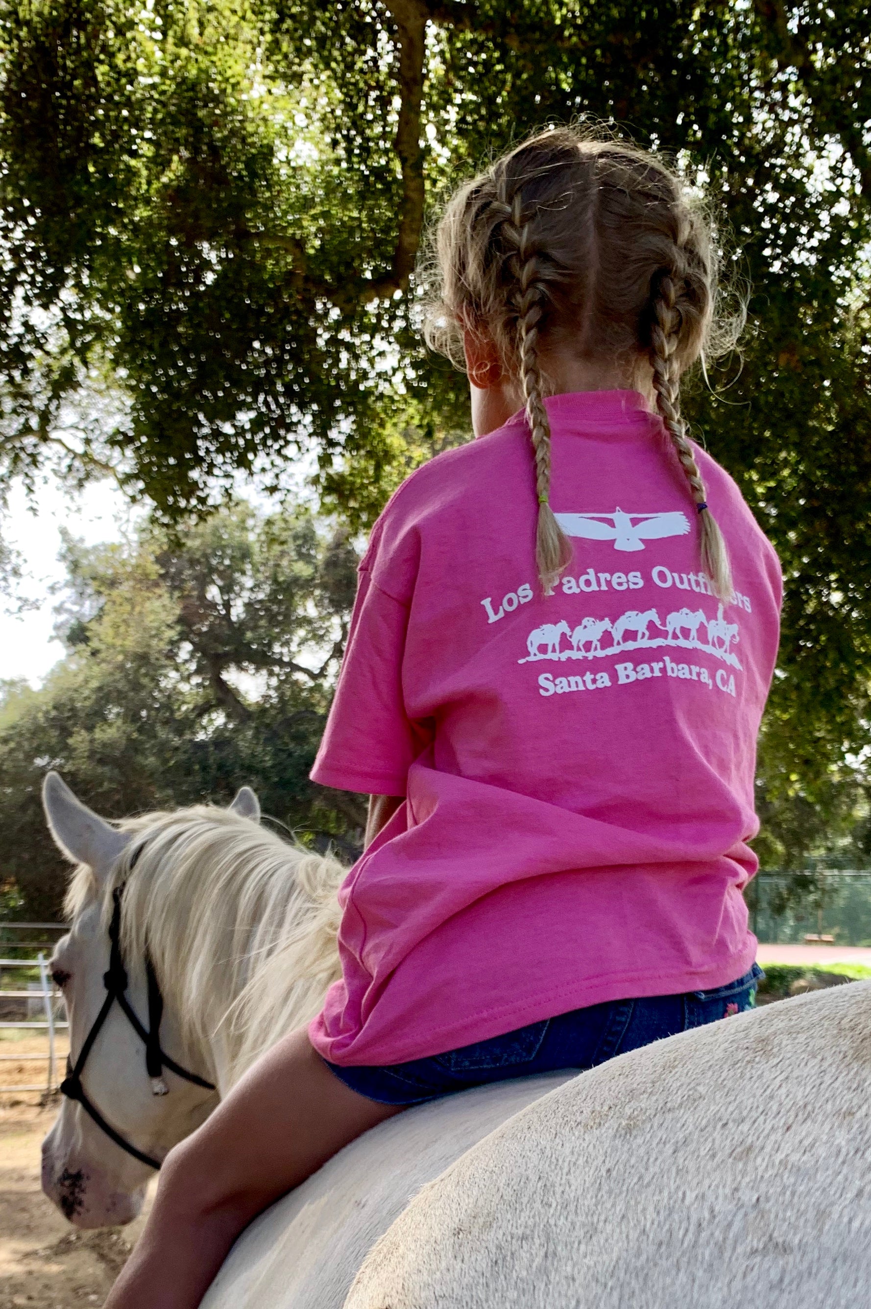Back view of little girl riding a horse outside wearing the comfortable pink cotton Kids Short Sleeve Tee